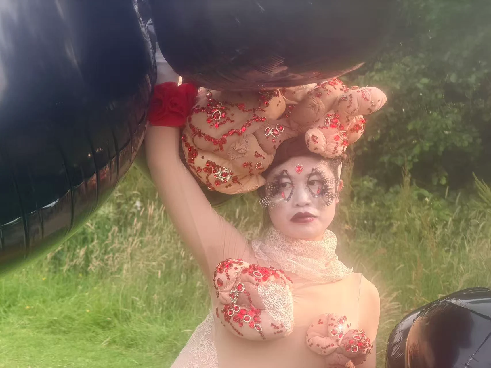 A Slice of the Crow: a performer beneath black balloons, wearing a jewelled sculptural headpiece